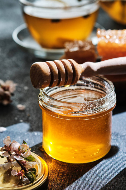 Een potje honing met honingraten en een stok, een theepot met een kopje  - Foto, afbeelding