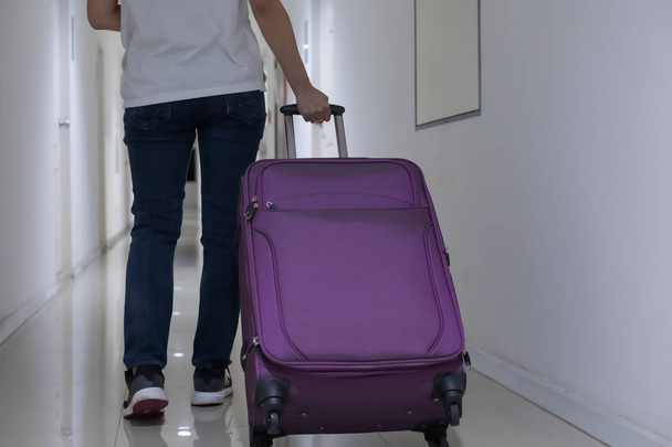 Młoda kobieta przeciągając purpurowy bagaż lub bagaż wzdłuż korytarza mieszkania - Zdjęcie, obraz