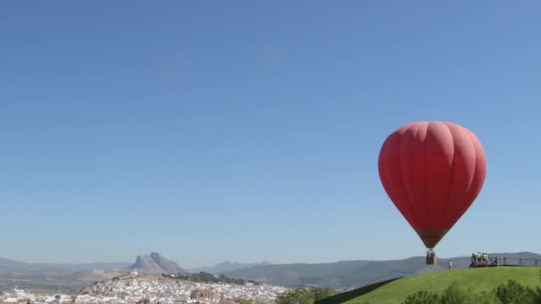 Červený horkovzdušný balón vzlétá s vesnicí Antequera v pozadí - Záběry, video