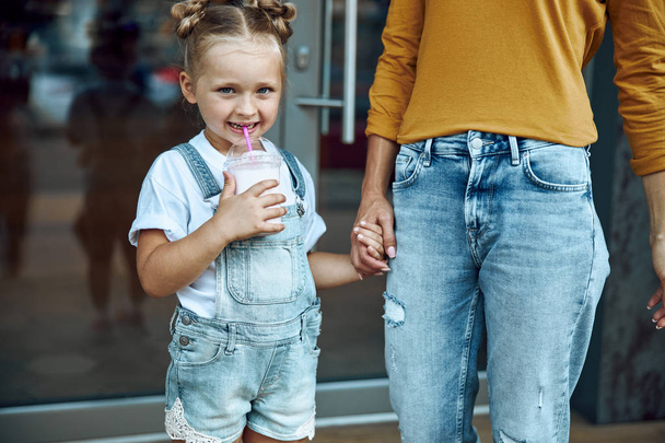 Girl standing with mother and enjoying milkshake stock photo - 写真・画像