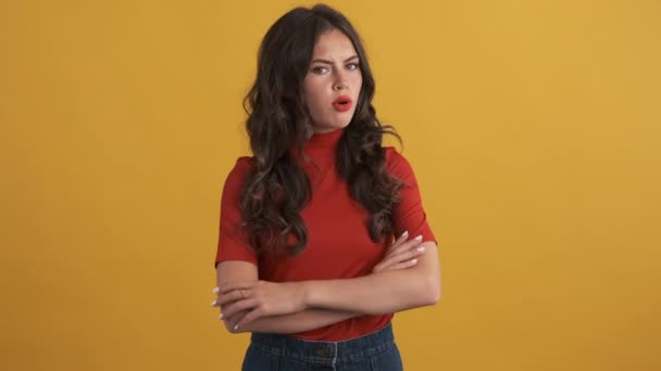 Serious brunette girl in red top confidently showing no gesture on camera over yellow background. No expression - Footage, Video