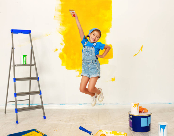 Repair in apartment. Happy child girl jumping paints wall - Photo, Image