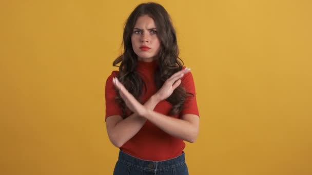 Serious brunette girl in red top angrily showing no gesture with crossed hands over yellow background - Footage, Video