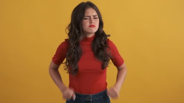 boos stemmig brunette meisje in rood top beledigend poseren op camera over gele achtergrond - Video