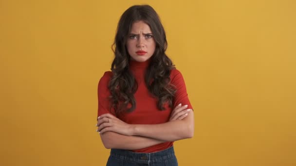 Zdenerwowany obrażony brunetka dziewczyna w czerwonym top niestety pozowanie z rąk skrzyżowanych na kamerze na żółtym tle - Materiał filmowy, wideo