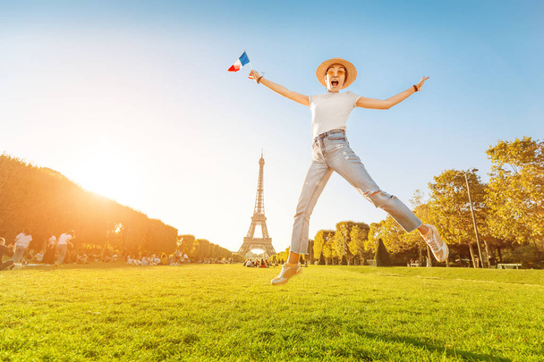 Ευτυχισμένος Ασιάτης/ισσα γυναίκα ταξιδιώτης άλμα με γαλλική σημαία στο Mars πεδίο στο φόντο του μεγαλοπρεπή πύργο του Άιφελ. Τουρισμός και τρόπος ζωής στη Γαλλία και το Παρίσι. Διακοπές στην Ευρώπη. - Φωτογραφία, εικόνα