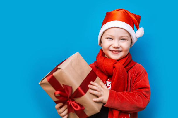 portrait of a happy little boy holding a new christmas gift with red ribbon in red clothes. happy new year, merry christmas - Фото, зображення