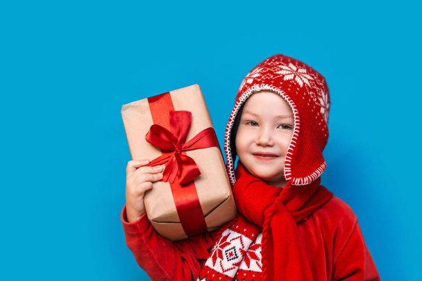 Portret van een gelukkige jongetje met een nieuwe kerstcadeau met rode lint in rode kleren. Gelukkig Nieuwjaar, Merry Christmas - Foto, afbeelding
