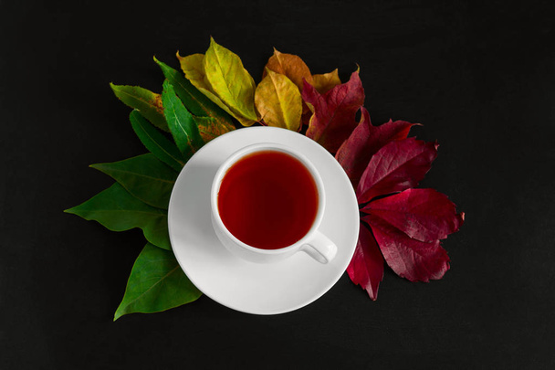 top view fall wallpaper with cup hot drink in a white cup and bouquet of autumn multicolored leaves on a black table background - Foto, Imagen