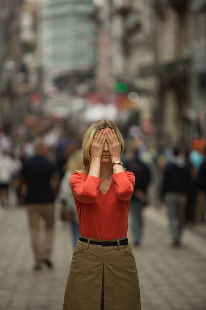 Panikattacke im öffentlichen Raum. Frau bedeckt seine Augen mit Händen, wenn er mitten auf einer belebten Straße steht. - Foto, Bild