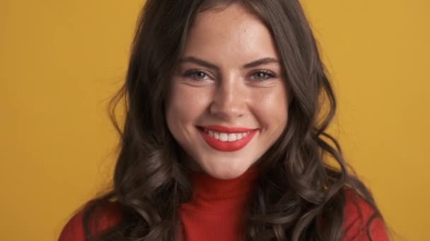 Porträt eines hübschen lächelnden brünetten Mädchens, das vor gelbem Hintergrund freudig in die Kamera zwinkert - Filmmaterial, Video