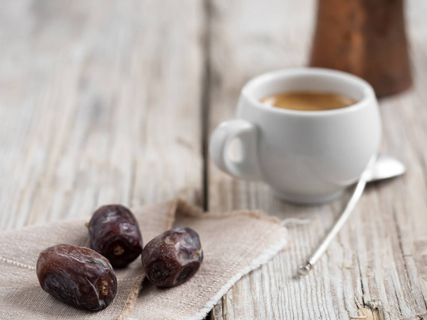 Aromatische koffie en oosterse dadels op een oude houten tafel. Een kopje espresso, op de voorgrond drie data van fruit. Close-up. - Foto, afbeelding