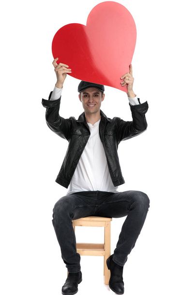 sitzender lässiger Mann mit einem großen roten Herz über dem Kopf glücklich - Foto, Bild