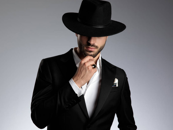 mysterieuze jonge elegante man dragen Tuxedo en zwarte hoed - Foto, afbeelding