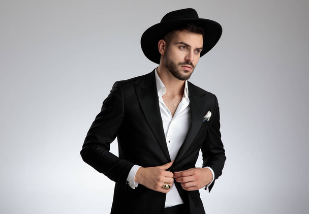 elegantní atraktivní mladý muž, který si uspořádával kabát na šedé pozadí - Fotografie, Obrázek