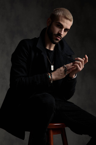 casual fashion man wearing black longcoat and touching hands - Fotó, kép