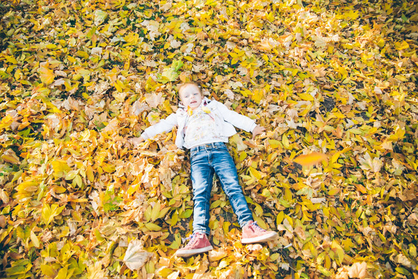 pequena menina deitado no chão em folhas amarelas
 - Foto, Imagem