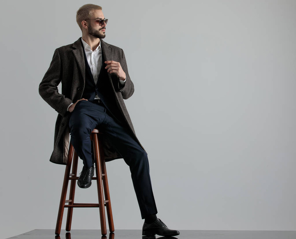 zakenman zitten met een been rusten en hand in zak - Foto, afbeelding