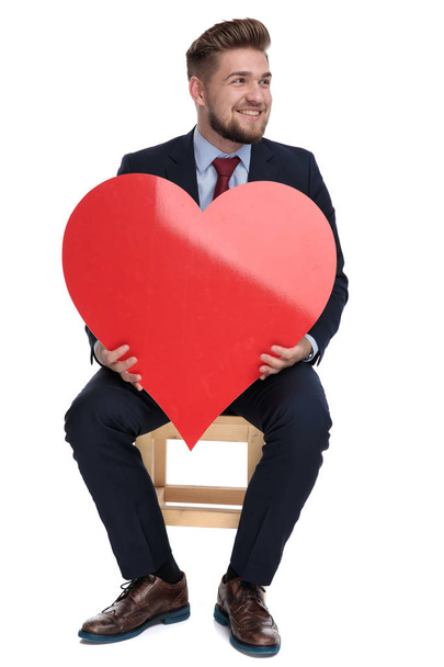 happy young businessman holding red heart in studio - Foto, afbeelding