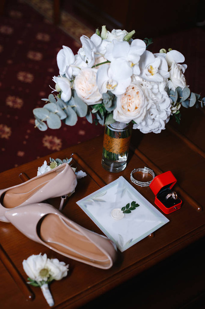 acessórios de casamento: buquê de noiva, duas casas de botão, sapatos femininos, alianças de casamento em uma caixa, pulseira feminina, envelope com um convite de casamento
 - Foto, Imagem
