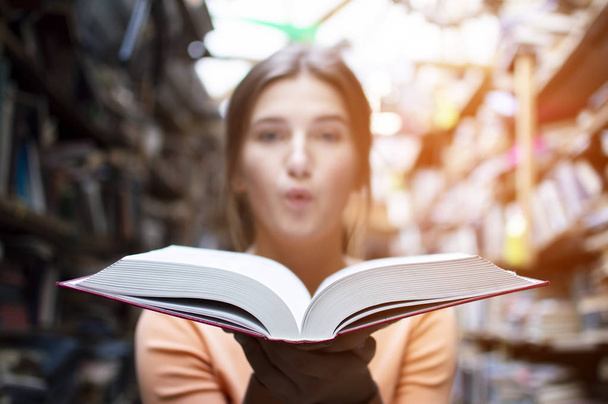 lány diák olvas egy nagy régi könyvet a könyvtárban, és fúj a por, közeli - Fotó, kép