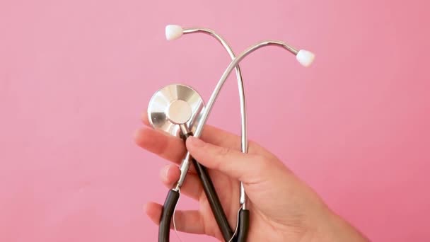 Stetoscopio o fonendoscopio semplice design minimale donna mano tenendo attrezzature mediche isolato su sfondo rosa pastello alla moda. Dispositivo strumentale per medico. Concetto di assicurazione sulla vita sanitaria - Filmati, video