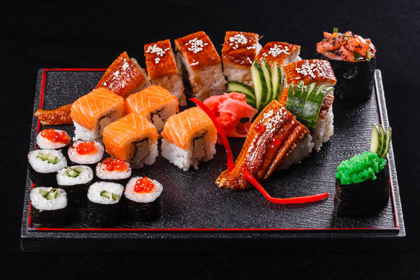 Suši drak s úhořem, okurkou a avokádem na černém pozadí. Japonské jídlo, chutné jídlo na oběd - Fotografie, Obrázek