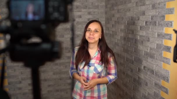 Uma jovem mulher em uma camisa de xadrez está falando na câmera em um fundo de tijolo. Mulher está gravando conteúdo para seu vlog. - Filmagem, Vídeo