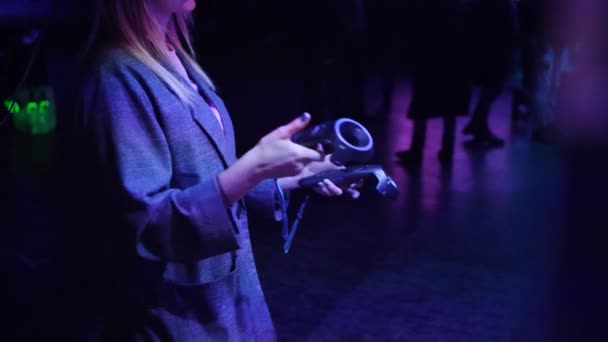 Woman in VR headset. Girl moves with controllers and light changes from violet to red - Materiaali, video