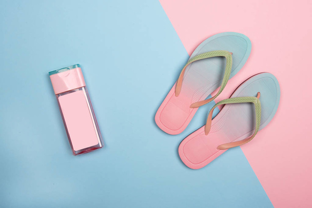 Stylish beach flip-flops and pink sunscreen bottle on pink and blue pastel background, top view. Summer concept with copy space. - Fotografie, Obrázek