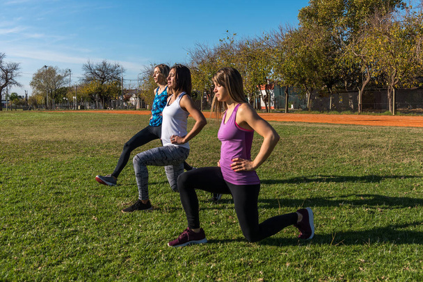 Tres mujeres caucásicas en el parque, dos rubias y una morena haciendo ejercicio en el parque. Concepto de deporte, salud y estilo de vida
 - Foto, Imagen