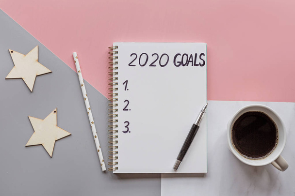 Happy New Year 2020. Desktop items with 2020 Goals in notebook, pen, straw, wooden stars, coffee on tricolour background. Top view, flat lay, overhead, copy space, mockup, template. Wishes and dreams - Foto, afbeelding