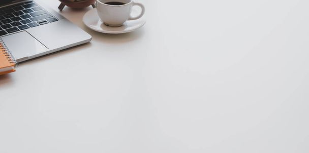 コピースペース付きの白い木製の机の上にラップトップコンピュータ、コーヒーカップ、事務用品を備えた最小限の職場  - 写真・画像
