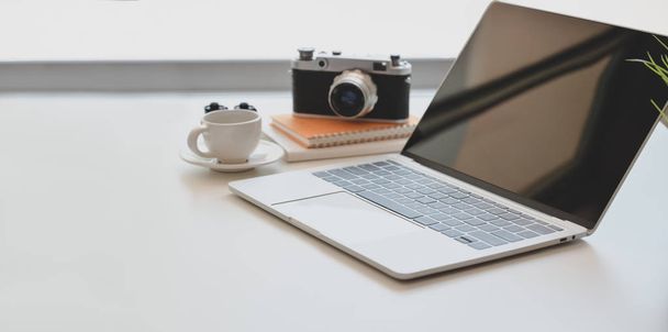 白い木製の机の上にオープンラップトップ、ヴィンテージカメラ、コーヒーのカップを持つ最小限の写真家の職場  - 写真・画像