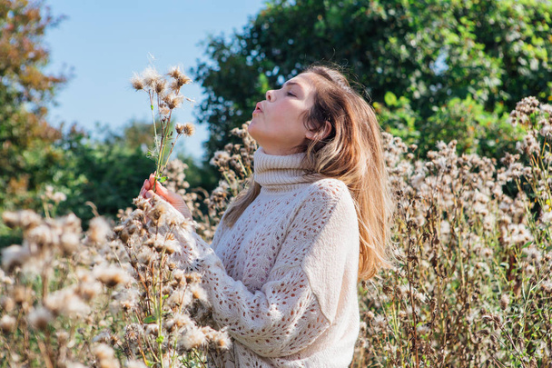 Portrait of a happy young beautiful woman in sweater and with dry agrimony. Woman blowing on dry bur - Fotografie, Obrázek