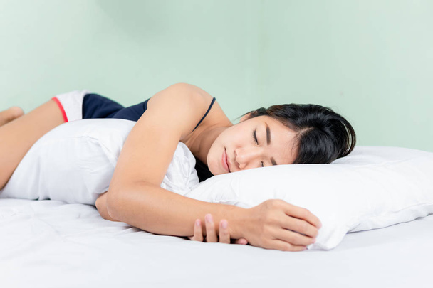 Mujer asiática acostada y durmiendo en la cama abrazando refuerzo. - Foto, imagen
