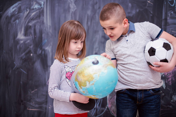 boy and little girl using globe of earth in front of chalkboard - Φωτογραφία, εικόνα