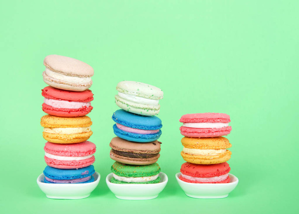 Biscoitos macaron em minúsculos pratos brancos empilhados em linhas graduadas, pastelaria francesa tradicional colorida em um fundo verde hortelã
. - Foto, Imagem