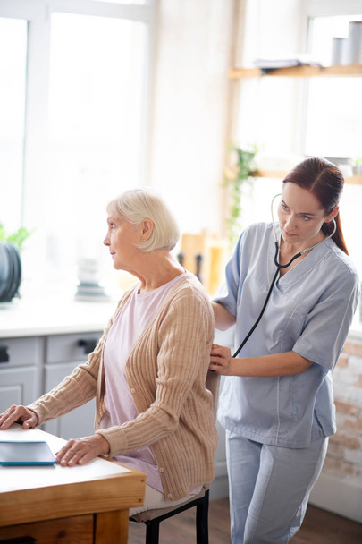 Nurse examining retired lady feeling sick and tired - Foto, imagen