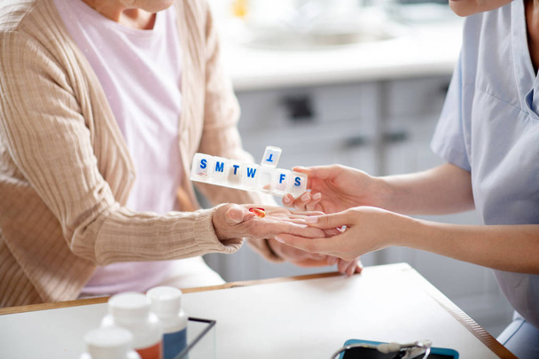 Caregiver putting pills on palm of retired woman - Foto, imagen