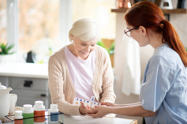 Pensioner taking vitamins standing near caregiver - Zdjęcie, obraz