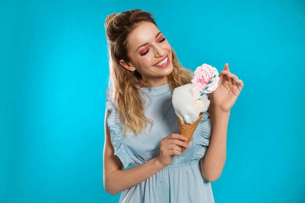Portrait of young woman holding cotton candy dessert on blue background - Zdjęcie, obraz