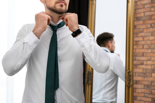 Businessman adjusting necktie near mirror in room, closeup - Fotografie, Obrázek
