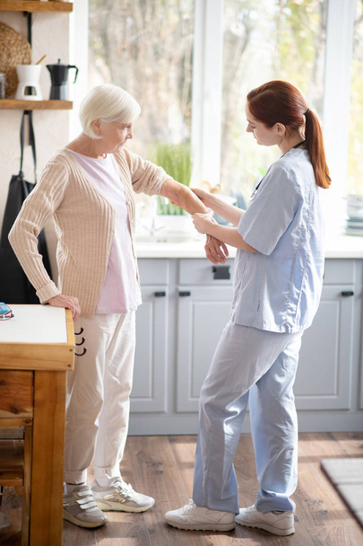 Pensioner having some ache in arm showing it to nurse - Zdjęcie, obraz