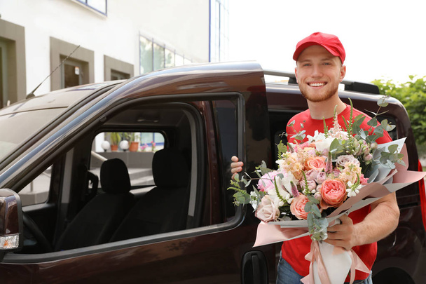 Delivery man with beautiful flower bouquet near car outdoors - 写真・画像