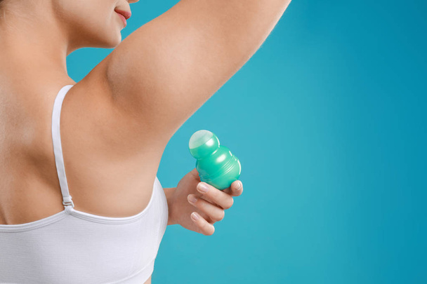 Young woman applying deodorant to armpit on teal background, closeup - Fotó, kép
