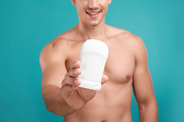 Young man with deodorant on light blue background, closeup - Φωτογραφία, εικόνα