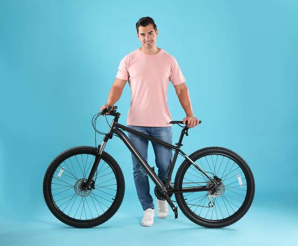 Handsome young man with modern bicycle on light blue background - Photo, image
