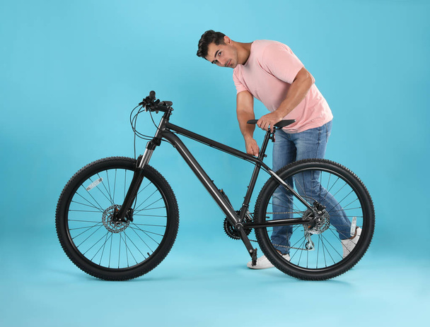 Handsome young man with modern bicycle on light blue background - 写真・画像