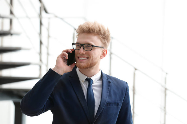 Portrait of handsome young man in elegant suit with glasses talking on mobile phone indoors - Foto, imagen